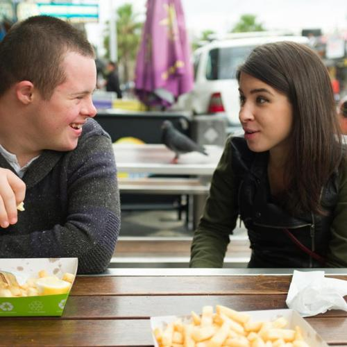 Two people sitting at an outdoor table talking and smiling, with food trays in front of them.