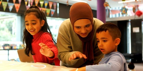 Woman and two children engaging with an interactive table in a classroom setting