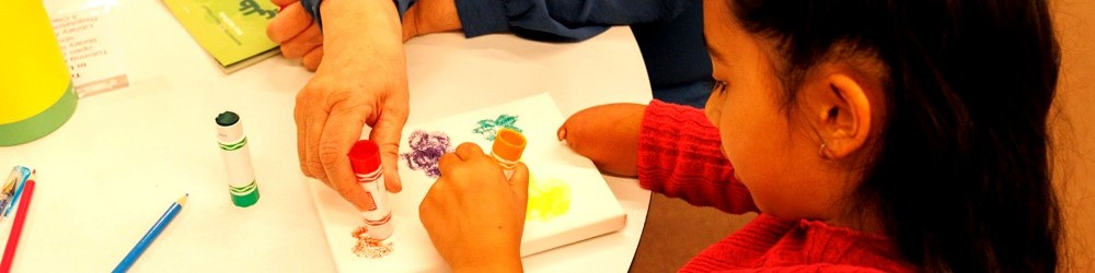 A child paints a small canvas with colourful stamps on a table in a warm setting.
