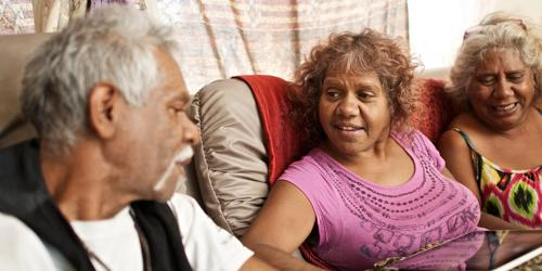 Three older adults sitting together on a couch, engaged in conversation.