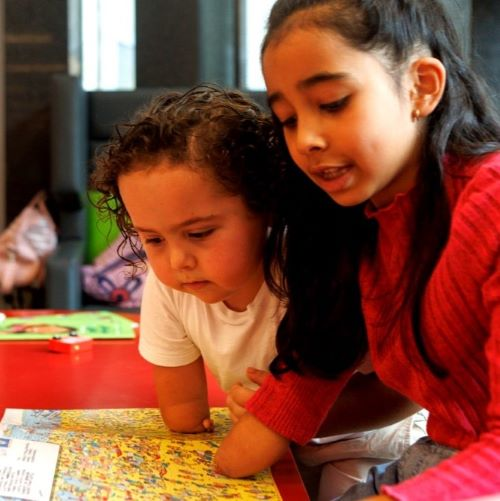 Two children leaning over a colorful map or book, concentrating closely.