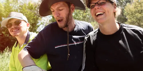 Three people outdoors smiling and laughing together in bright sunlight.