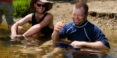 Two men sitting in shallow water, smiling and enjoying time together.
