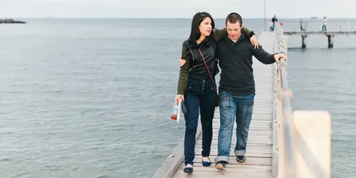 Couple walking arm in arm along a pier over the water.