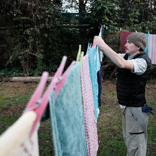 Man hanging laundry on an outdoor clothesline in a backyard.
