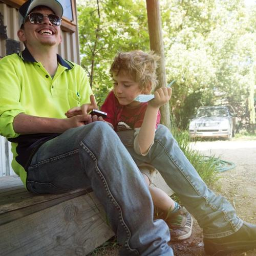 Man and young boy sitting on a porch, smiling and looking at a phone together.