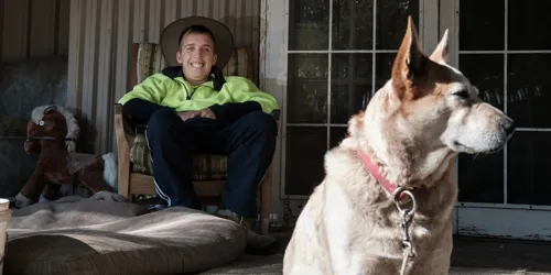 Man relaxing on a porch while a large dog sits in the foreground.
