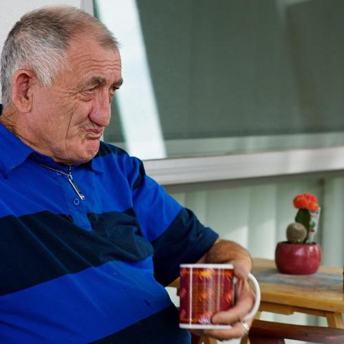 Older man sitting with a mug in hand, looking thoughtful outdoors.