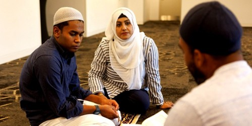 Three people seated on the floor, listening and reading together during a quiet learning session.
