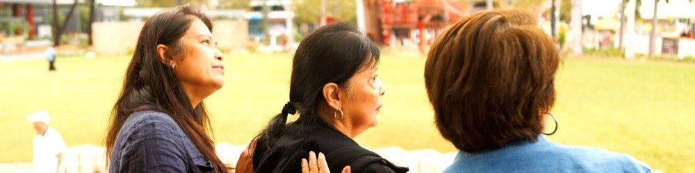 Three women standing outdoors, looking ahead across a park.