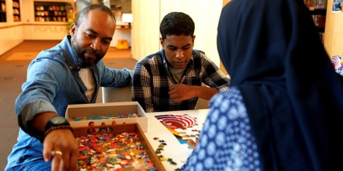 Three people working together on a colorful jigsaw puzzle at a table.