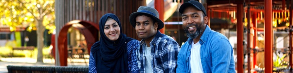 Three people sitting together in a park, smiling at the camera.