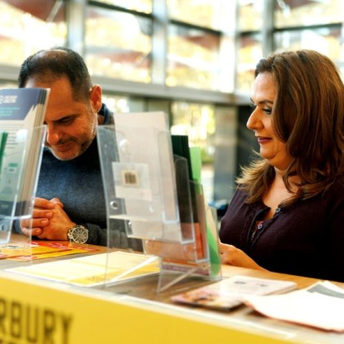 A man and woman at a library desk looking at brochures or reading materials.