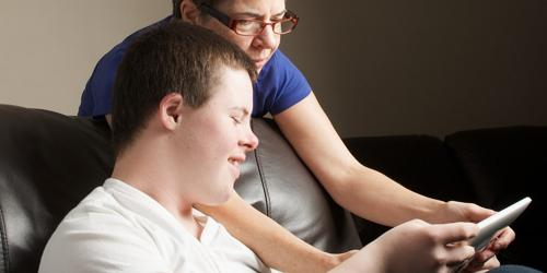 Woman helping a teenager use a tablet while sitting on a couch.