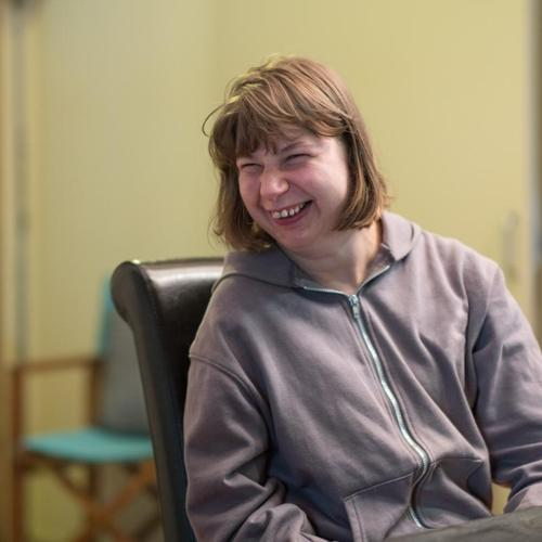 Woman sitting indoors smiling and looking off to the side, relaxed and cheerful.
