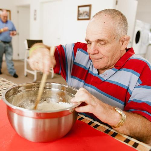 Older man stirring mixture in a bowl at a table while baking.