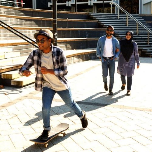 A young person skateboarding in a plaza while two adults walk behind.